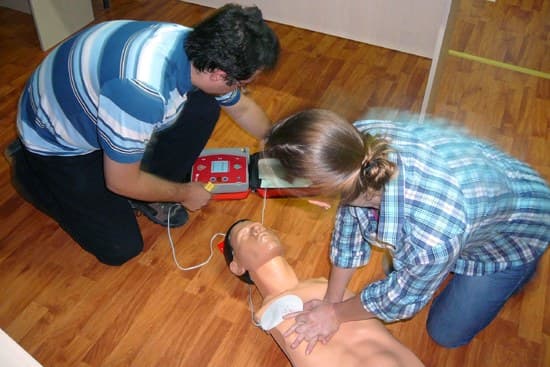 Cursanți exersând resuscitarea pe un manechin, cu defibrilatorul alături