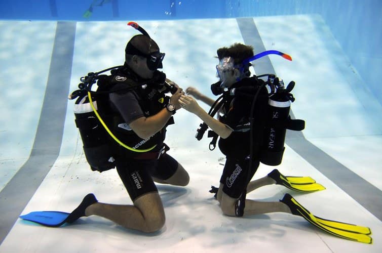 Instructor verificând echipamentul unui cursant sub apă