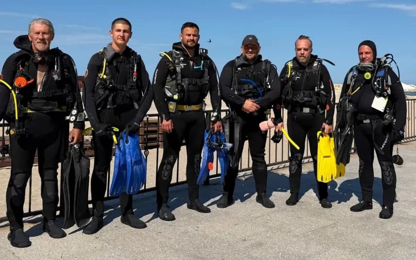 Șase scafandri în costume de neopren, cu labele în mână, pe digul de la Eforie Sud